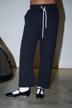 black sweatpants with white socks and black shoes against a white wall and concrete floor