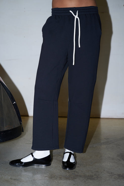 black sweatpants with white socks and black shoes against a white wall and concrete floor