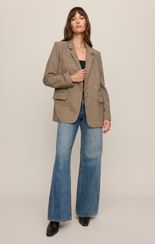 Woman wearing a patterned blazer and blue jeans on a plain background