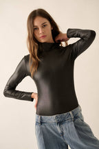 Woman wearing a black long-sleeve top and blue jeans against a plain background