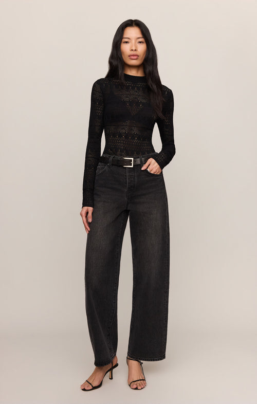 Woman wearing a black long-sleeve top and black jeans on a plain background