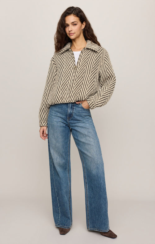 Woman wearing a patterned shirt and blue jeans on a plain background