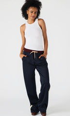Woman wearing a white tank top and navy pants on a white background
