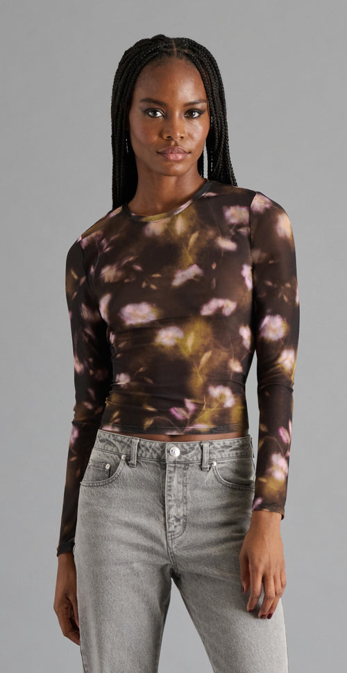 Person wearing a long-sleeve floral top and gray jeans against a gray background