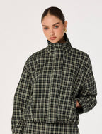 A model wearing a black and olive green plaid puffer jacket with a high collar, photographed against a solid off-white background.