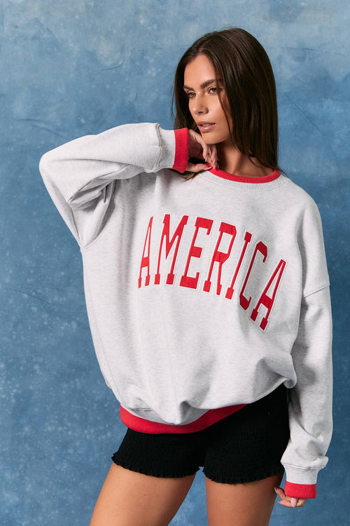 Woman wearing a gray sweatshirt with 'AMERICA' printed in red on a blue background