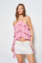 Woman wearing a pink ruffled top and white skirt against a white background