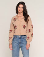 Woman wearing a beige cardigan with floral patterns and blue jeans on a plain background