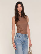 Woman wearing a brown sleeveless top and blue jeans against a plain background