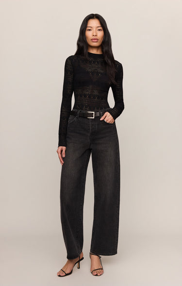 Woman wearing a black long-sleeve top and black jeans on a plain background