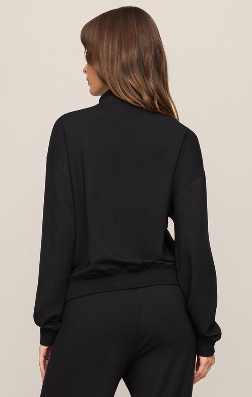Woman wearing a black long-sleeve top and pants on a beige background
