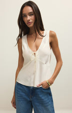 Woman wearing a white sleeveless top and blue jeans against a plain background