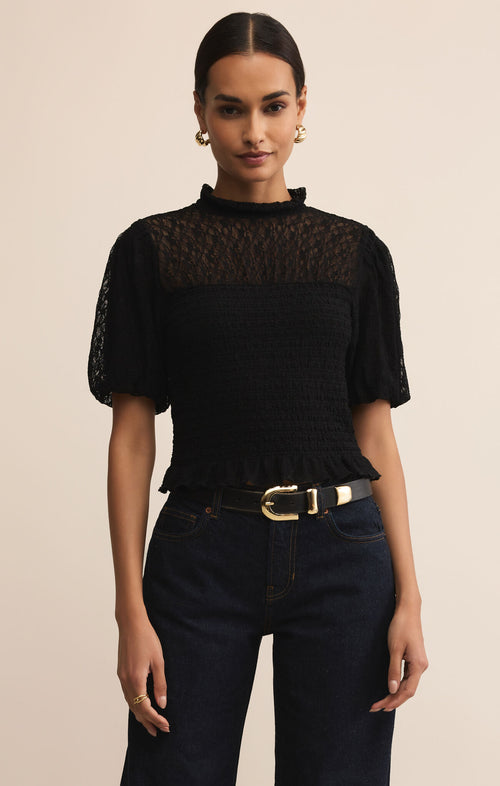 Woman wearing a black lace top and dark jeans with a beige background