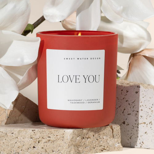 Red candle with 'Love You' label in front of white flowers