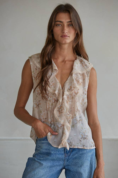 Woman wearing a sleeveless patterned top and blue jeans against a plain background