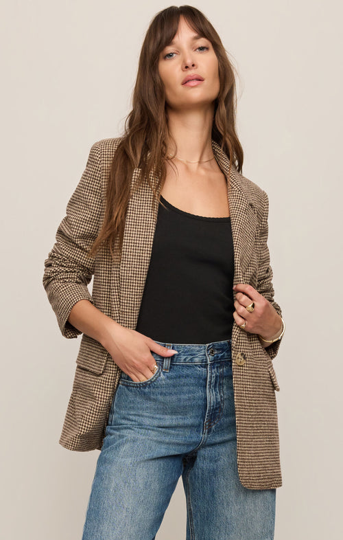 Woman wearing a brown checkered blazer, black top, and blue jeans on a beige background