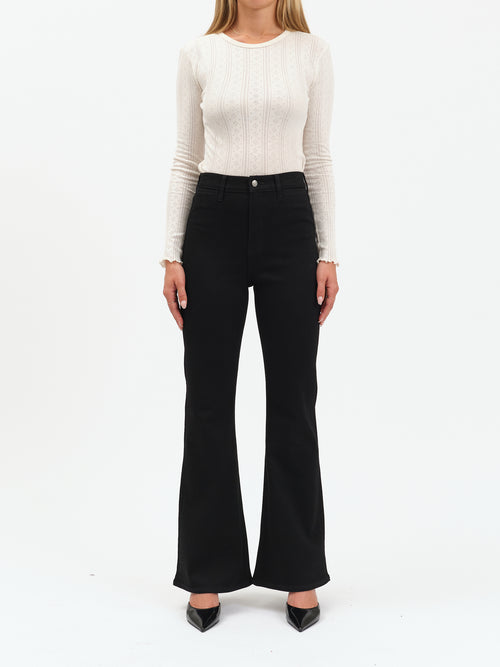 Person wearing a white long-sleeve top and black flared pants on a white background