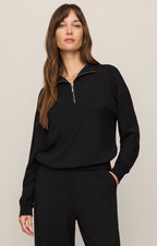 Woman wearing a black long-sleeve top with a zipper on a beige background