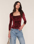 Woman wearing a burgundy velvet top and blue jeans against a plain background