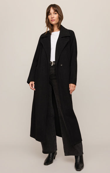Woman wearing a long black coat on a plain background