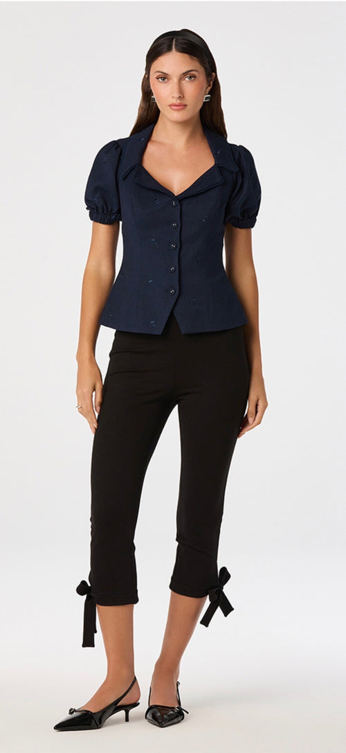 Woman wearing a navy blue top and black pants with bow details on a white background