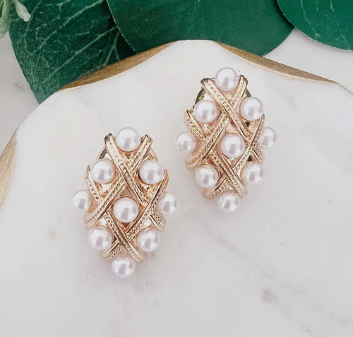 Pair of gold earrings with pearl accents on a white stone surface with green leaves in the background.