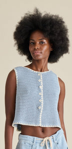 Woman wearing a light blue crochet top with white buttons against a beige background