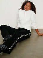 Woman wearing a white sweater and black pants with white stripes sitting on a concrete floor.