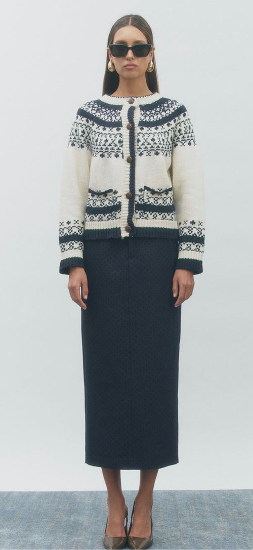 A model wearing a cream and navy knit cardigan with a Fair Isle pattern, paired with a dark navy midi skirt and sunglasses, standing against a light gray studio background.