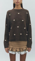 Brown sweater with floral embellishments worn by a model on a white background
