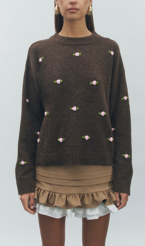 Brown sweater with floral embellishments worn by a model on a white background