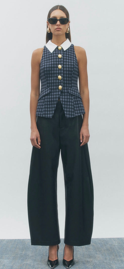 A model wearing a sleeveless navy and black gingham button-front top with a white pointed collar and gold buttons, paired with black wide-leg trousers and black pointed heels.
