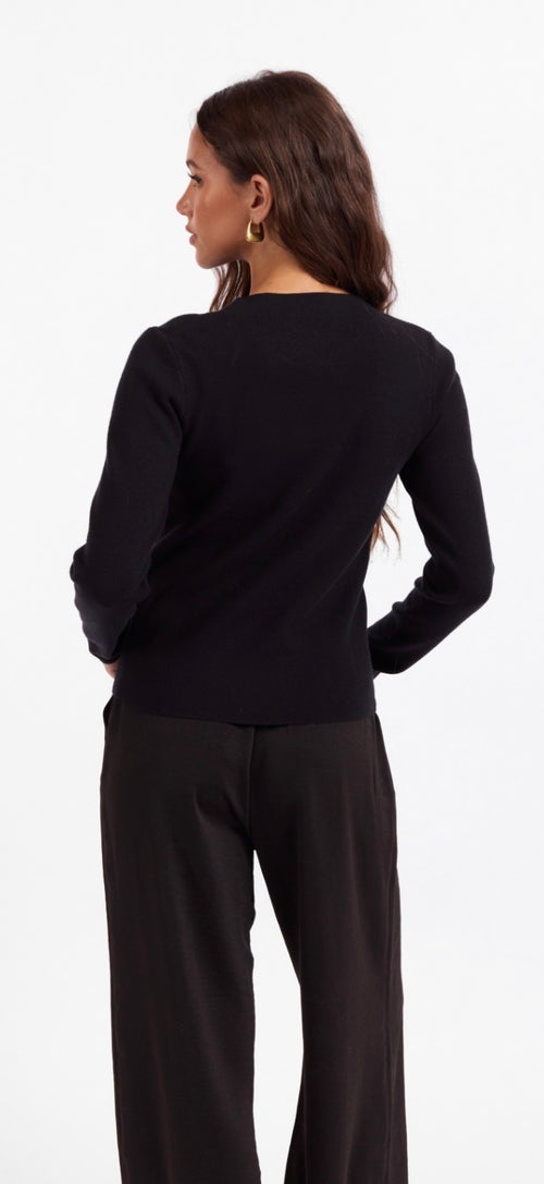 A woman shown from the back wearing a black long-sleeve top and black wide-leg pants against a plain white studio background.