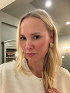 Woman with blonde hair wearing a white sweater and gold earrings indoors.