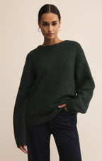 Woman wearing a dark green sweater and dark pants against a beige background