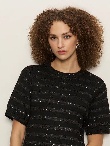 Woman wearing a black dress with white stripes and black patent leather boots against a plain background